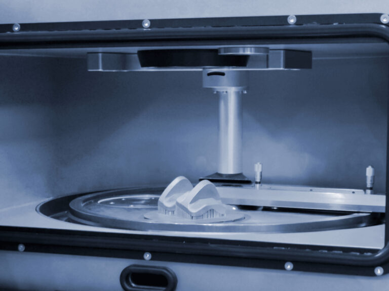 Close-up view of a 3D printer in operation, showcasing the creation of a complex object on a circular build platform with a vertical support structure above it.